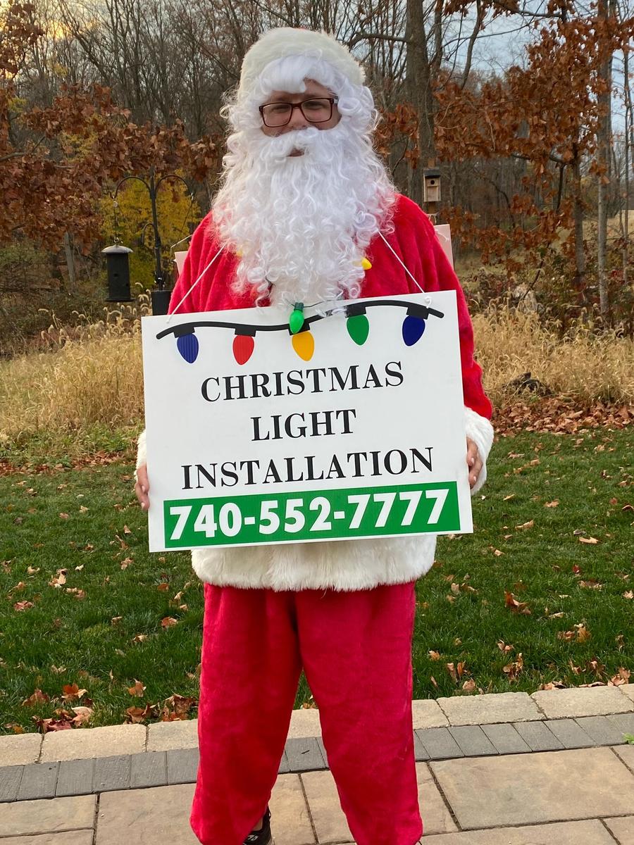 Santa holding the Deck The Homes Christmas light installation sign with the company phone number